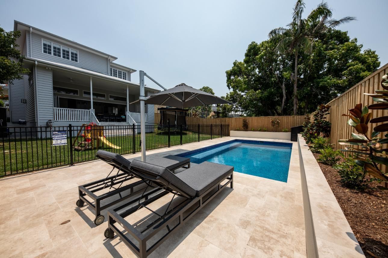 Backyard patio with a swimming pool, lounge chairs, and a house in bright sunlight