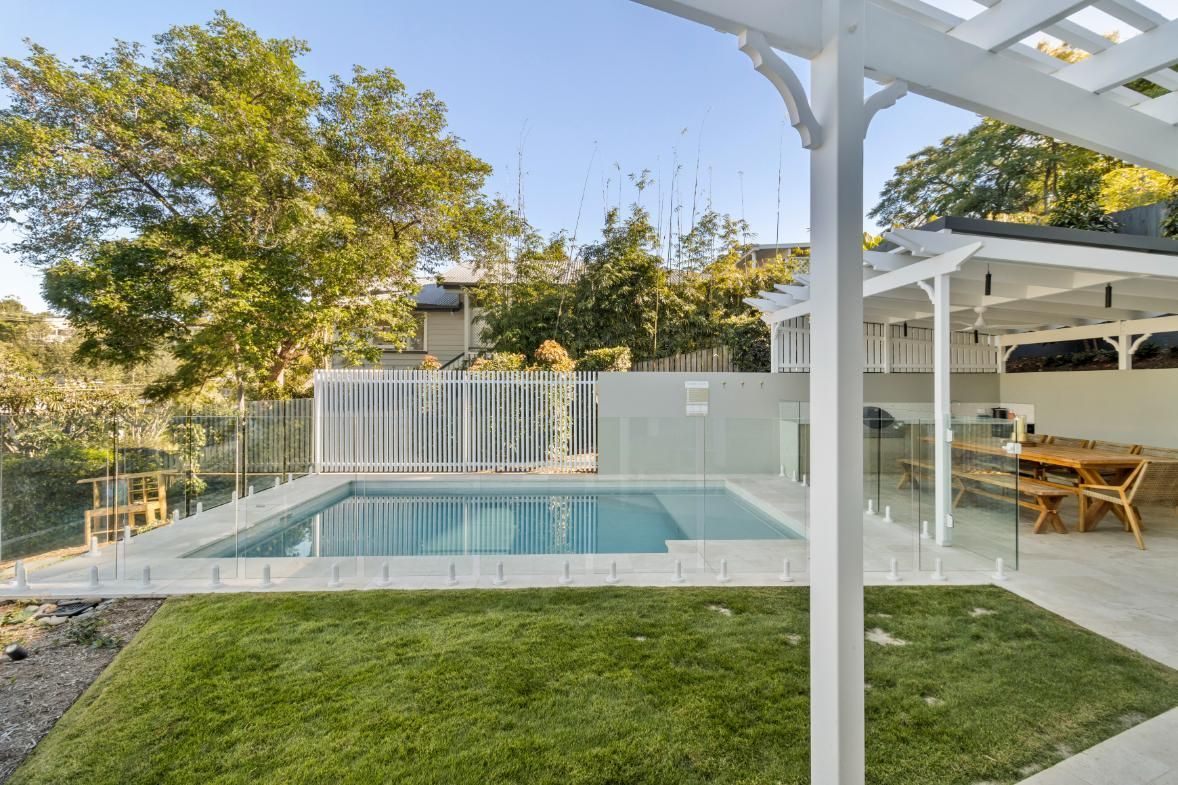 Backyard pool with white pergola, patio seating, and green lawn in bright daylight