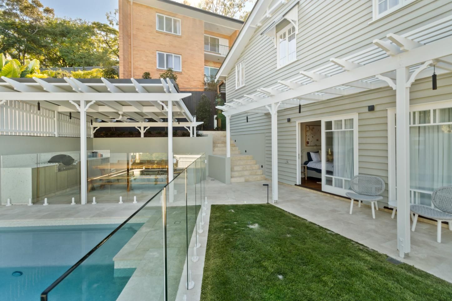 Modern backyard with pool, glass fence, white pergola, and house patio with sliding doors