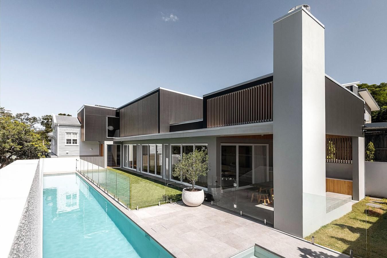 Modern two-story house with dark trim, front fence, and green trees under a blue sky