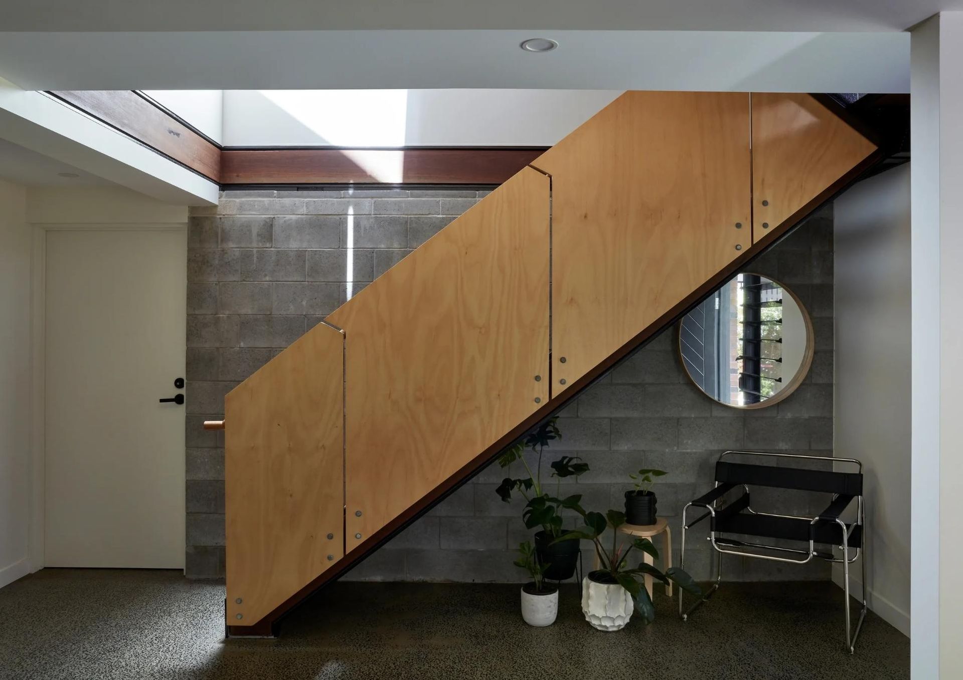 Wood-paneled staircase with glass railing in a modern interior, beside a mirror and potted plants