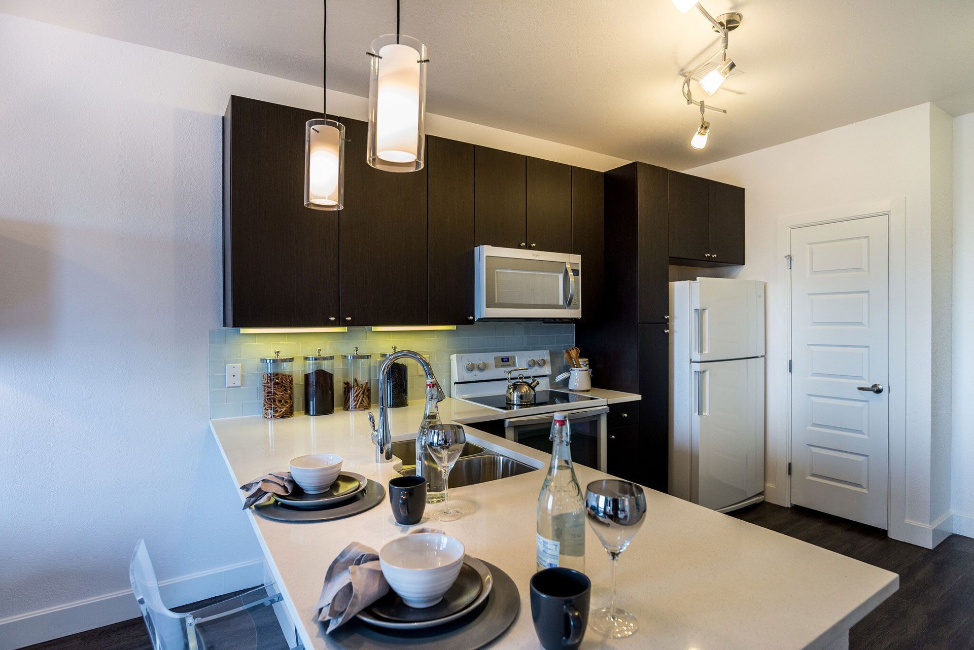 Modern apartment kitchen with dark wood cabinets, stainless steel appliances, and a white island.