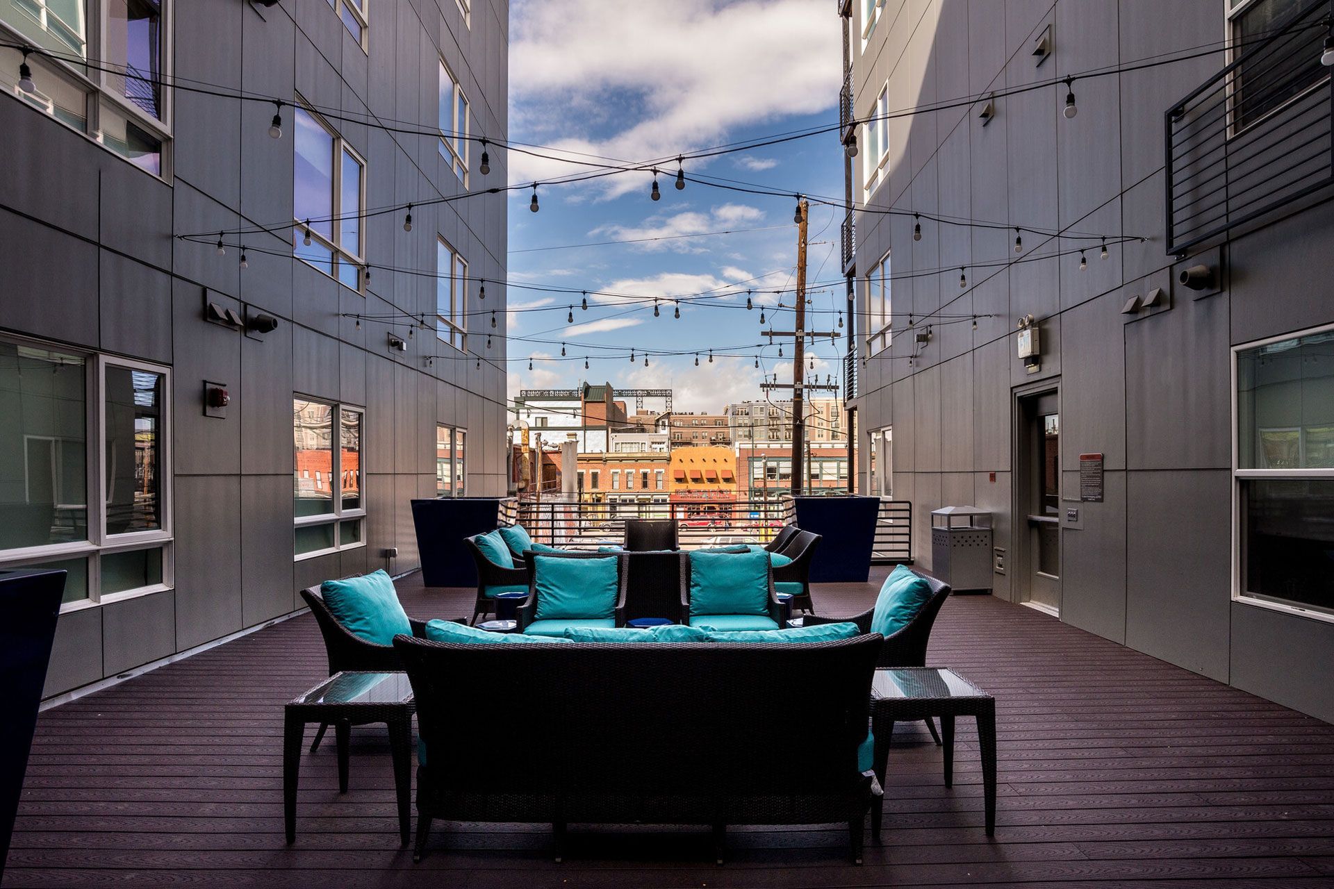 Rooftop community lounge on a wooden deck with teal cushions and string lights.