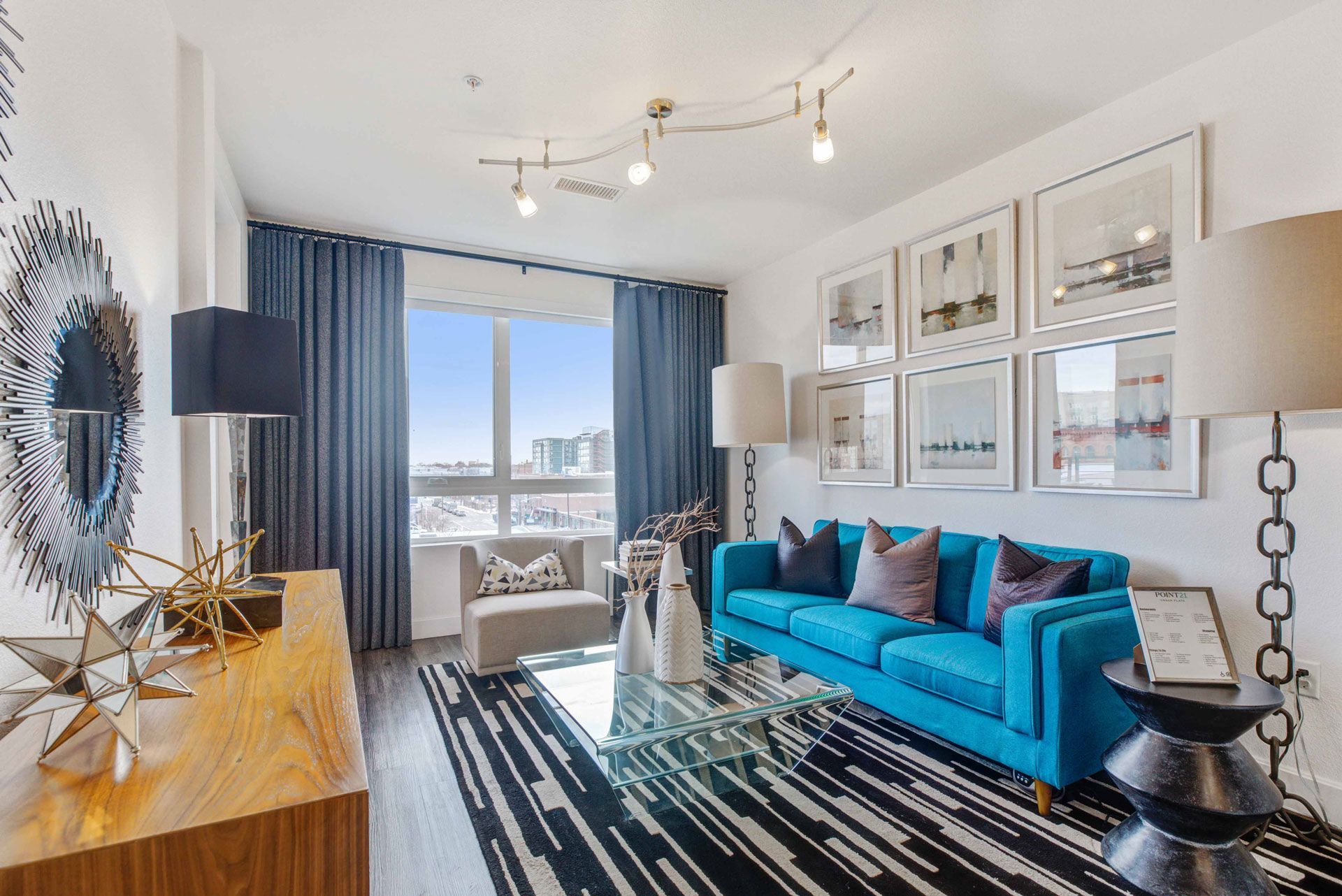 Bright modern living room with a blue sofa, glass coffee table, and wall art.