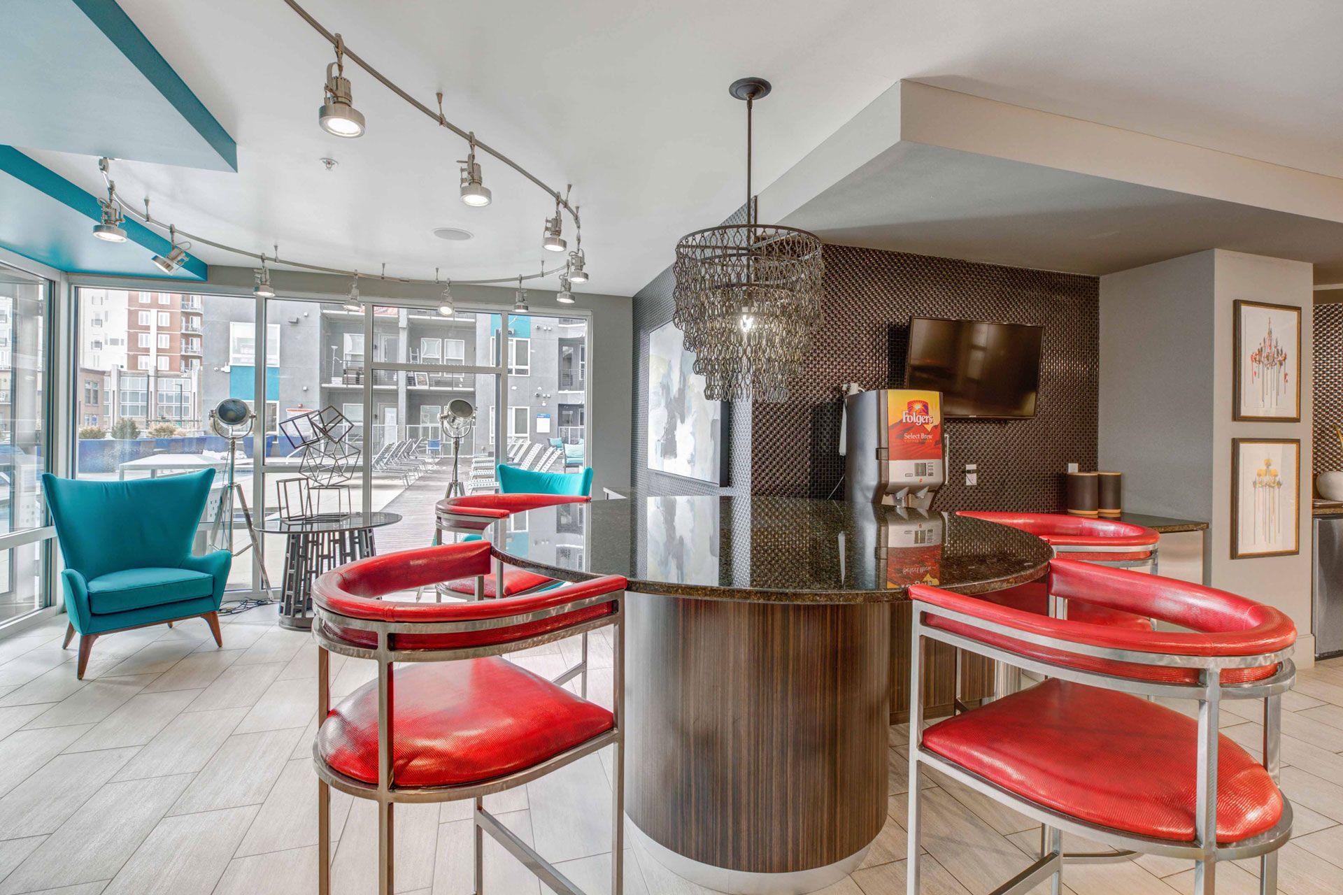 Modern community lounge with curved bar, red seats, teal chairs, and large windows.