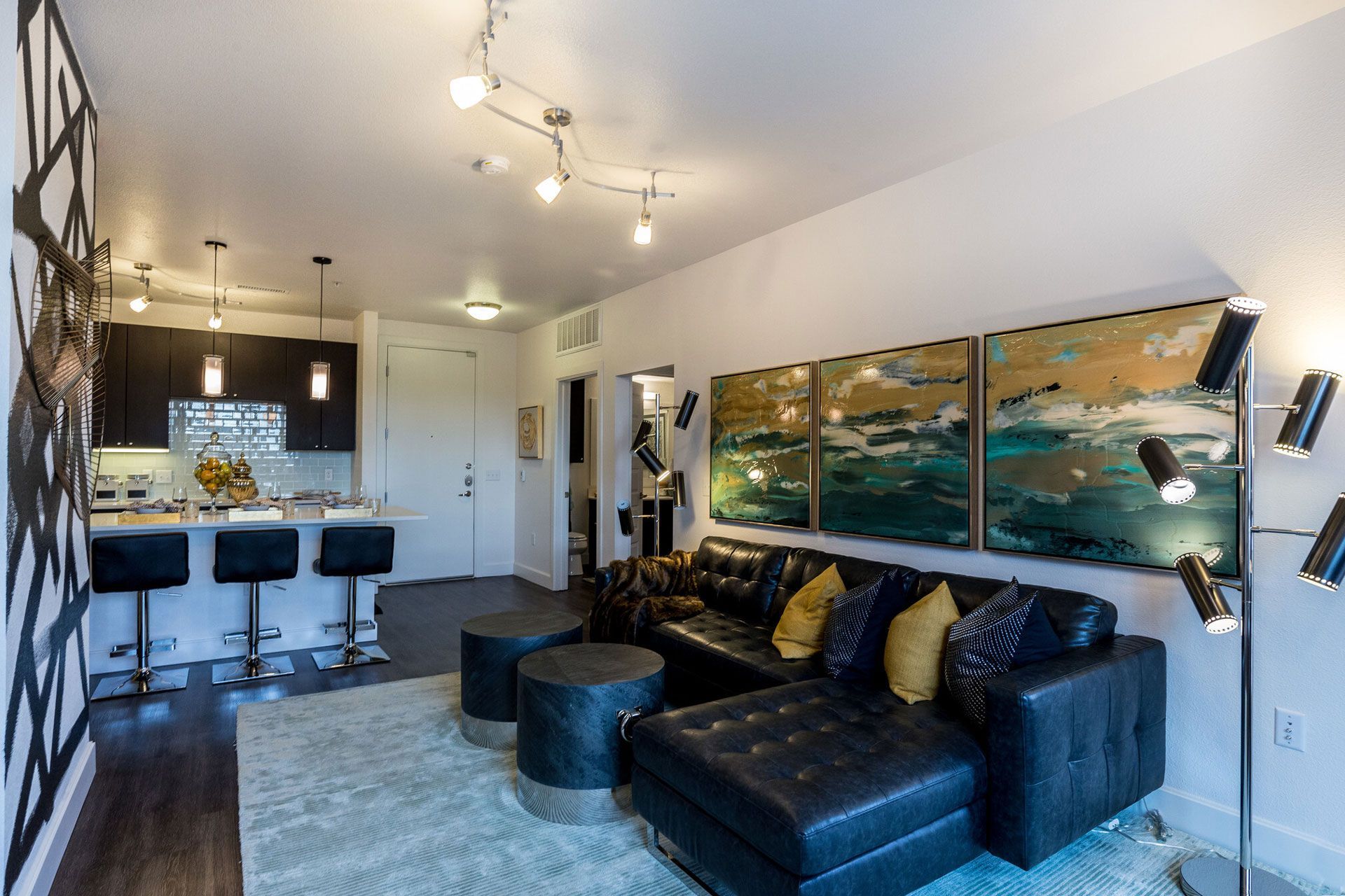 Open-concept apartment living room with a leather sectional, kitchen island, and abstract wall art.