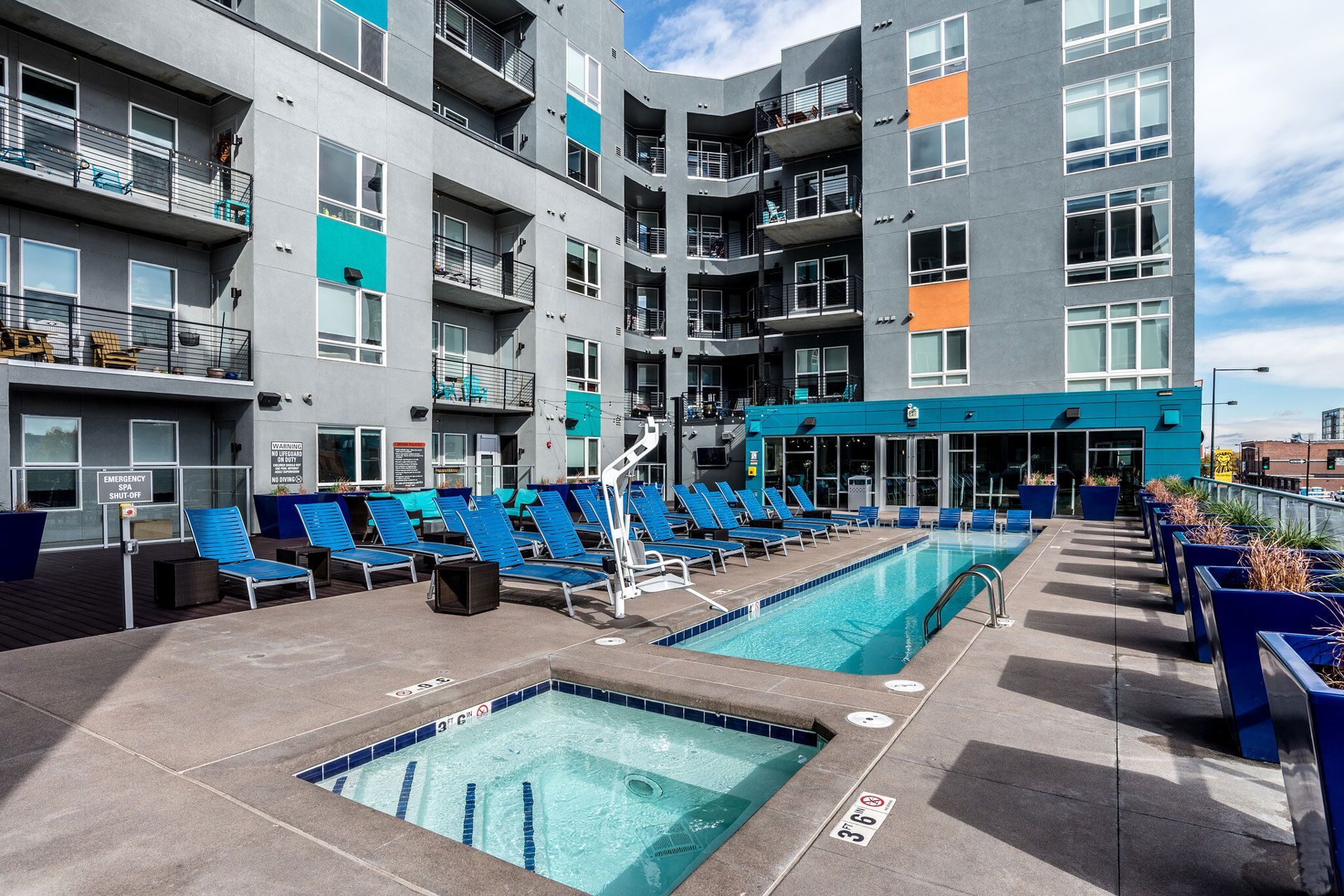 Outdoor apartment pool deck with blue loungers and a modern building backdrop.
