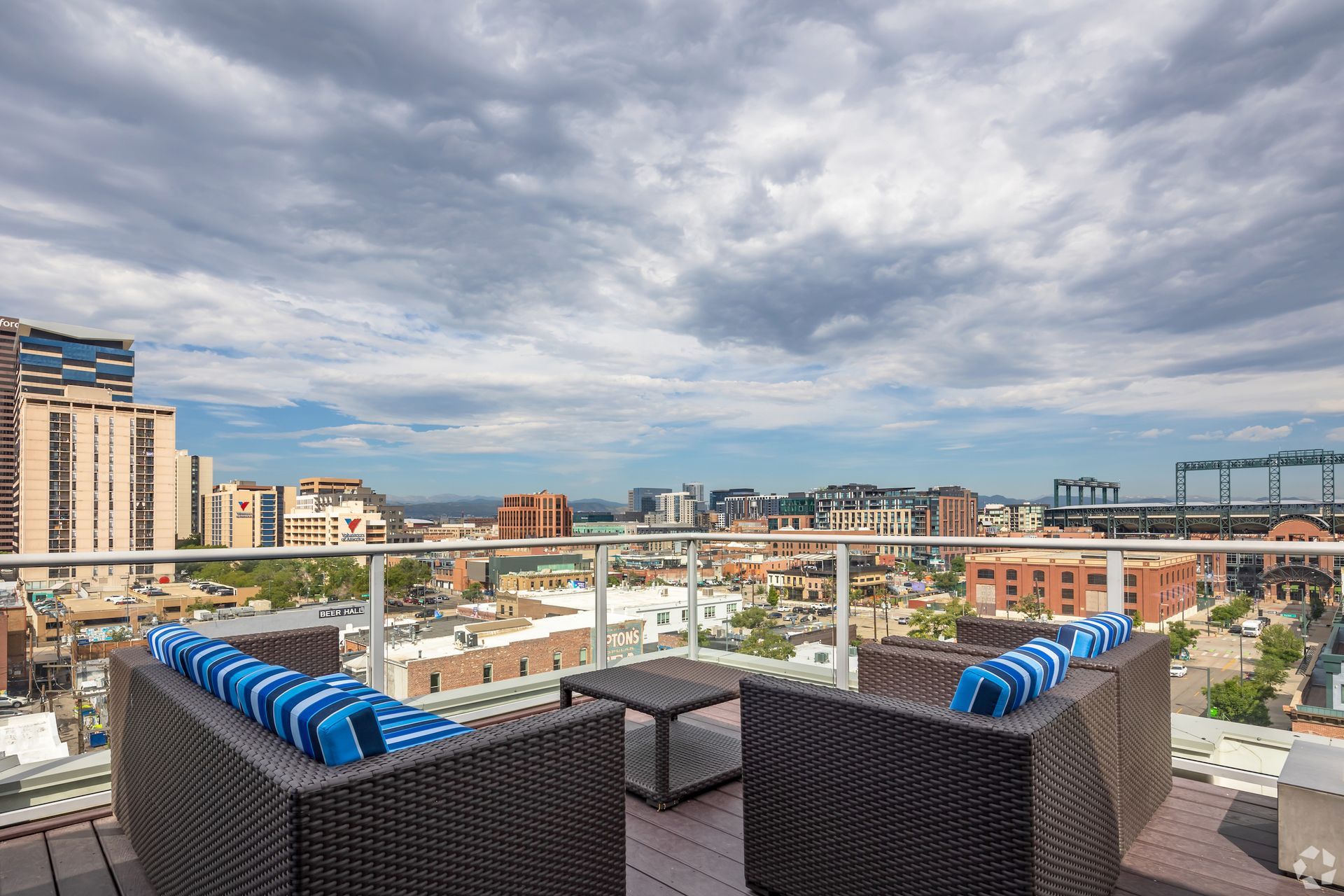Rooftop terrace with dark wicker seating and blue-striped cushions overlooking city skyline.
