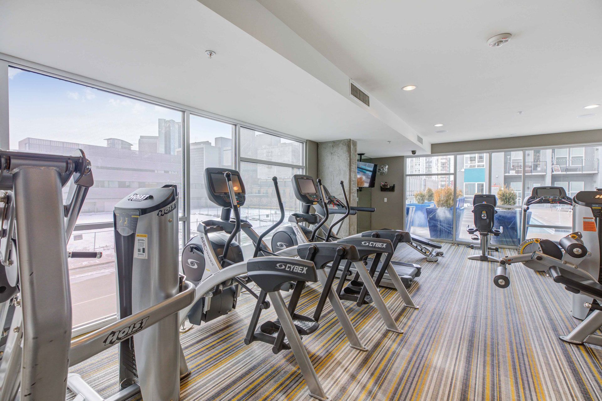 Modern resident gym with treadmills and ellipticals by large windows.