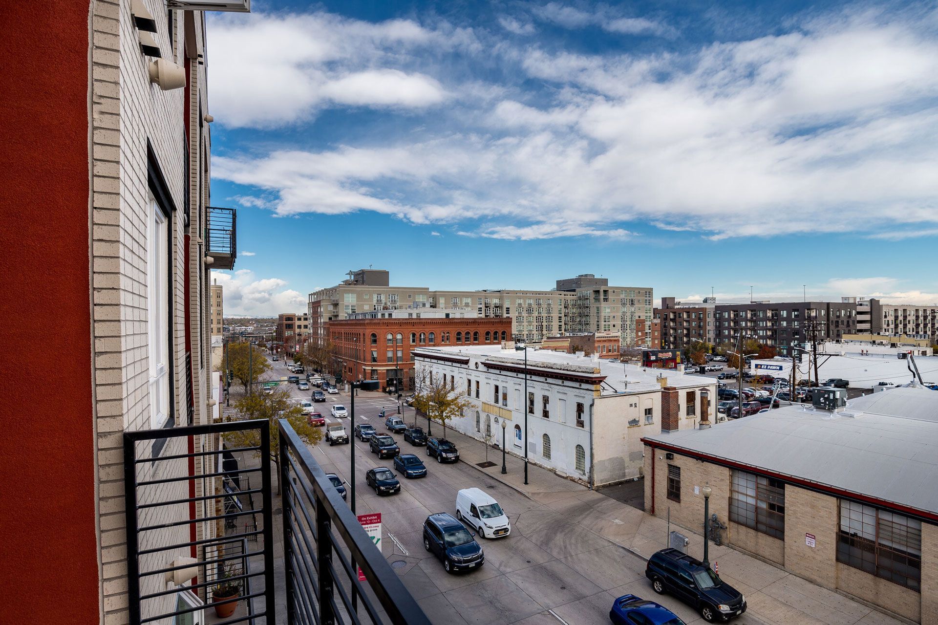 View from an apartment balcony of a city street with parked cars and nearby buildings.