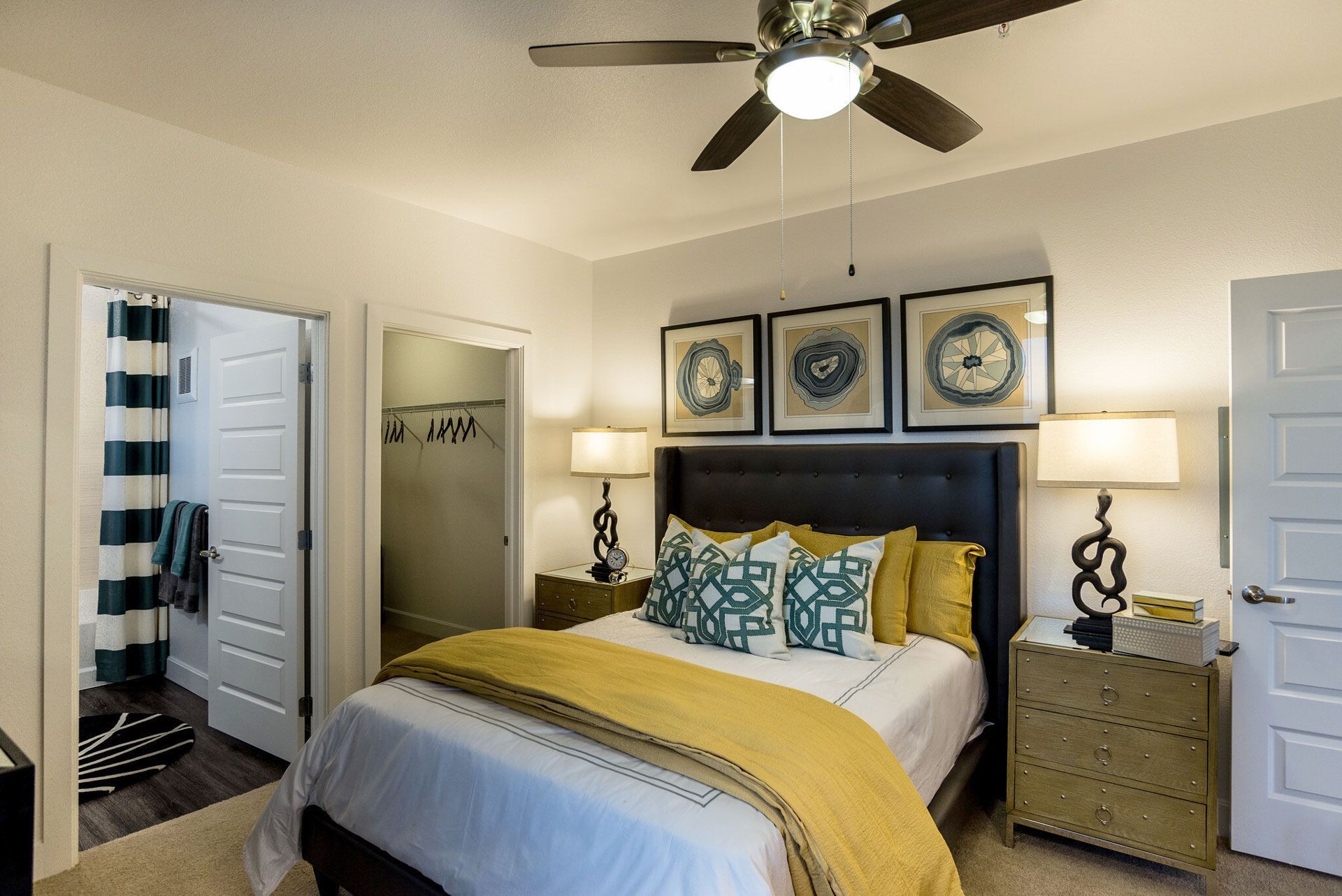 Furnished bedroom with an upholstered headboard bed, yellow accents, two nightstands, lamps, and wall art.