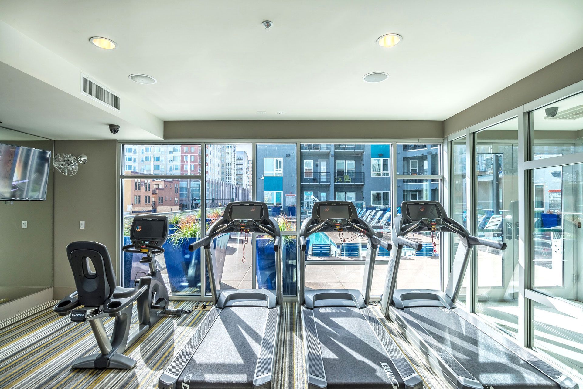 Bright indoor fitness center with four treadmills and a wall-mounted TV.