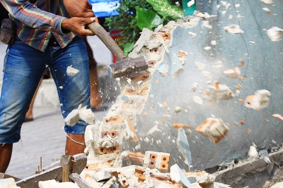 A man is breaking bricks with a hammer.