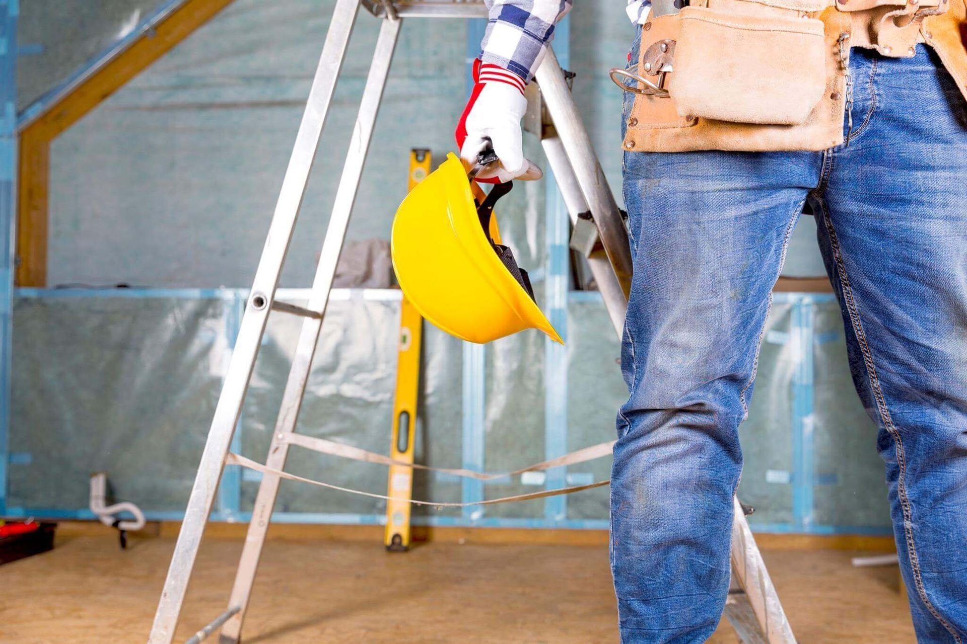 A construction worker is standing on a ladder holding a hard hat.