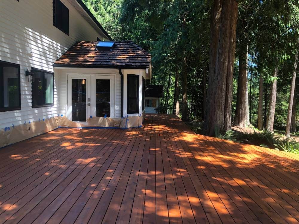 A large wooden deck is in front of a house surrounded by trees.