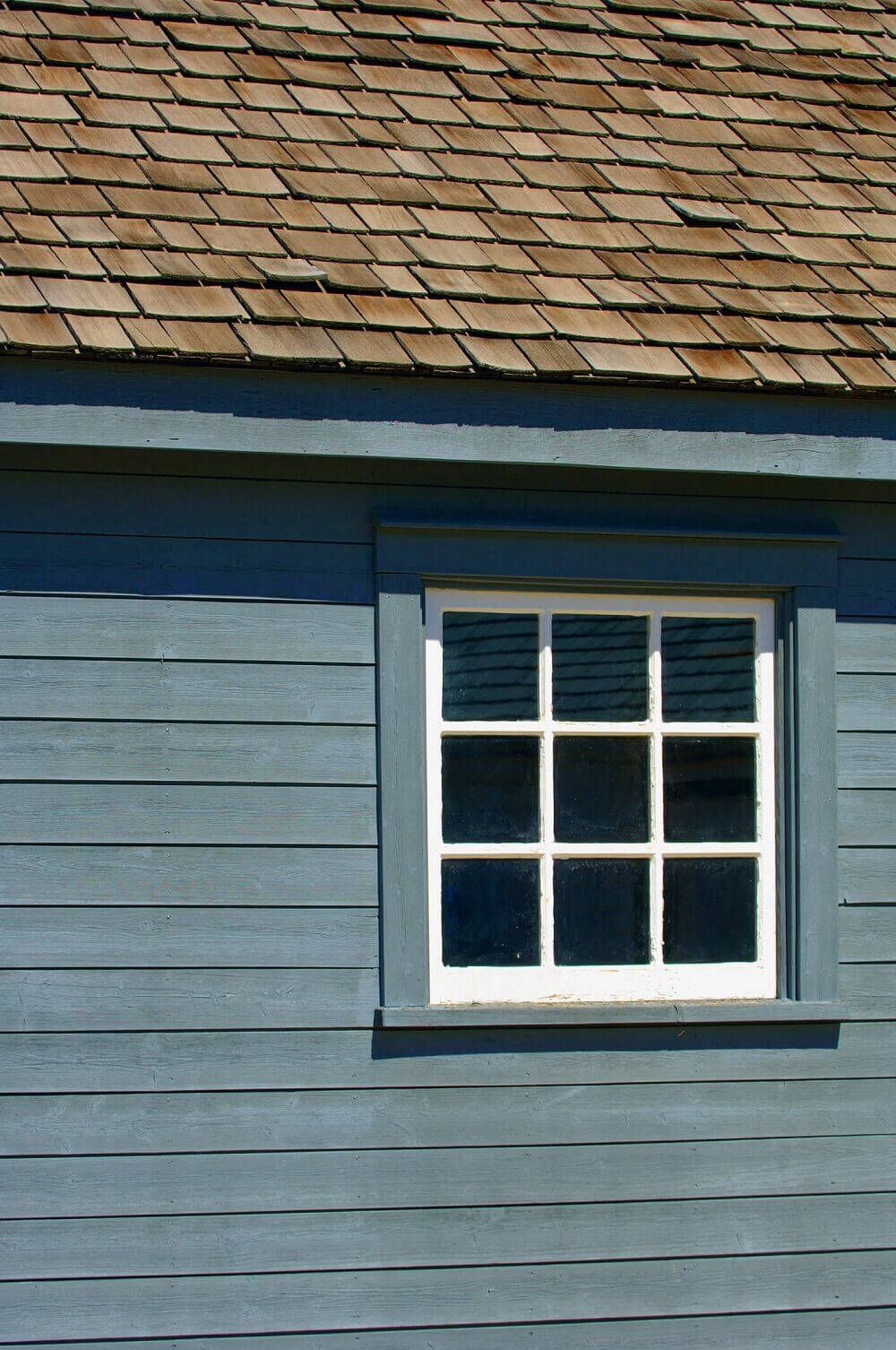 A blue house with a white window and a wooden roof