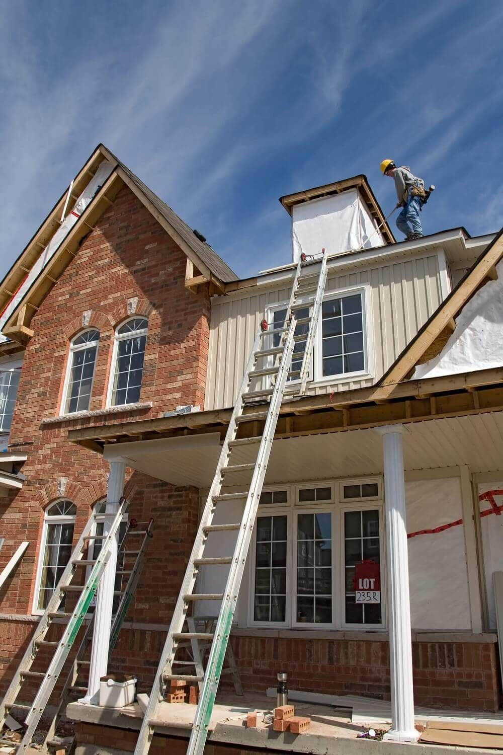 A man is standing on the roof of a house under construction.