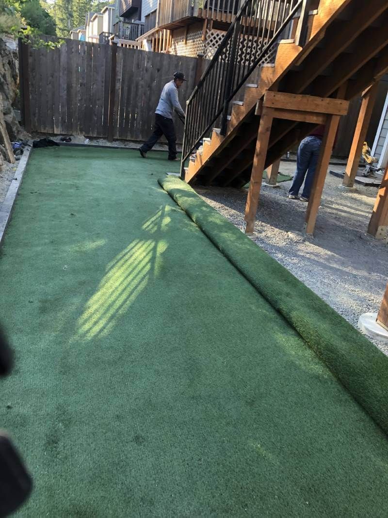 A man is laying artificial grass in a backyard.