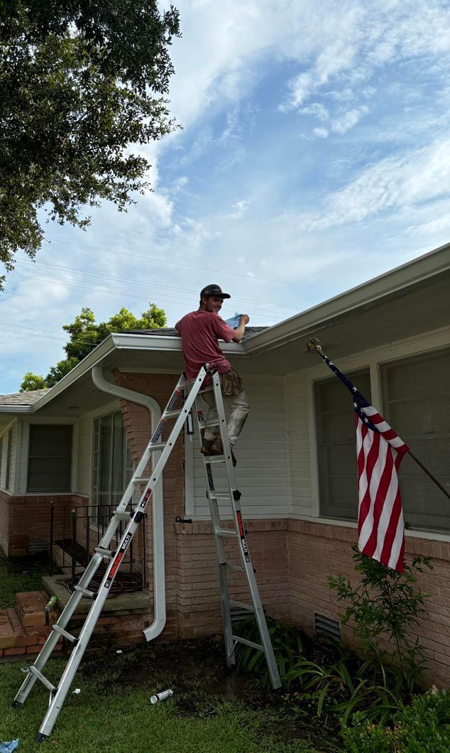 A man is standing on a ladder working on the roof of a house.