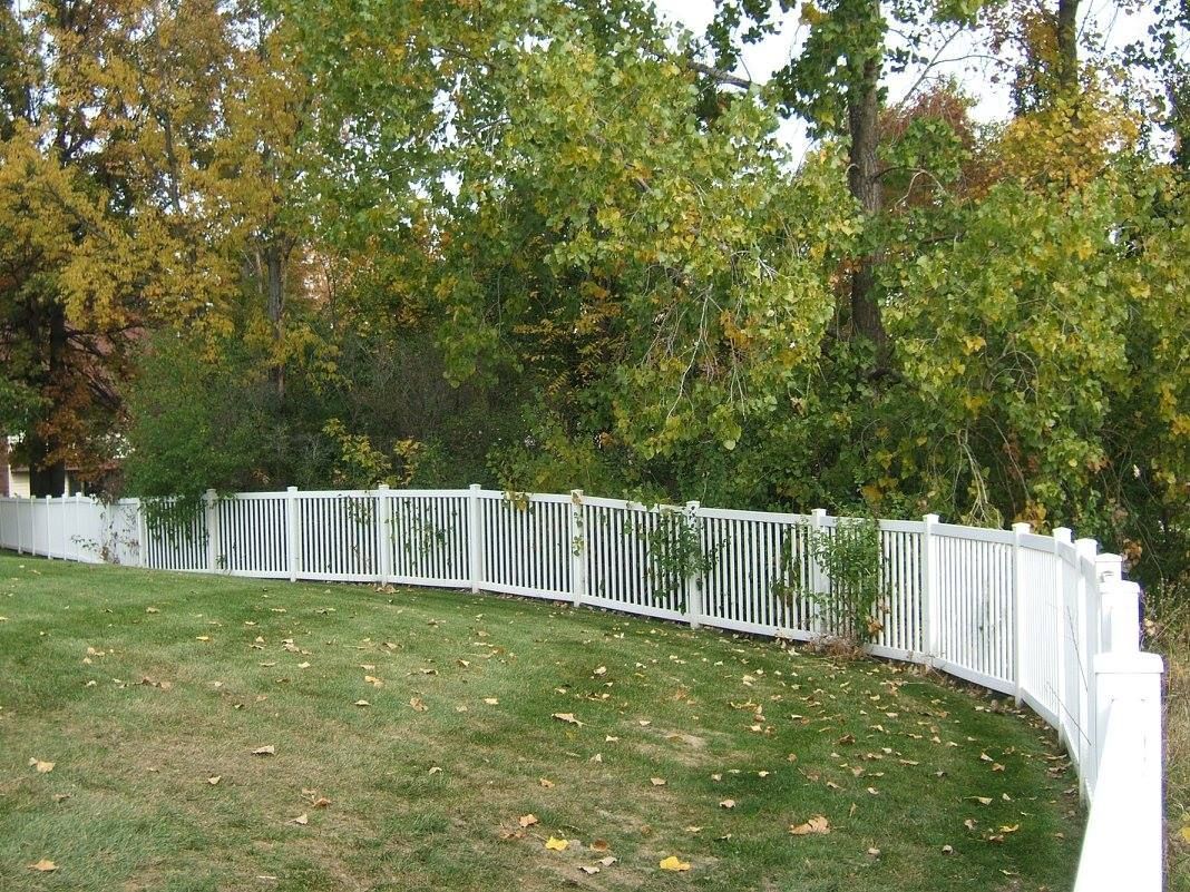 A white vinyl fence runs across a landscaped backyard with lawn and blue sky in the background.