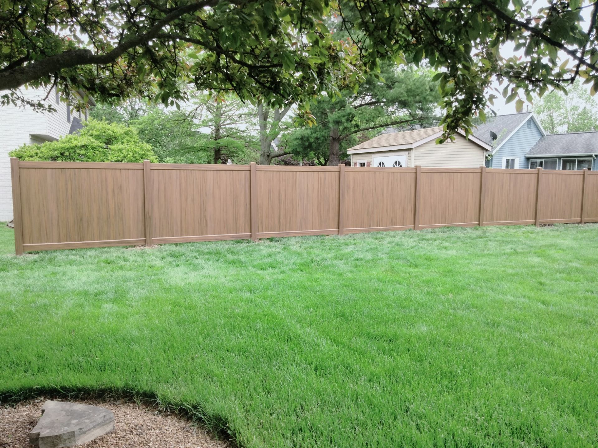 A wooden fence around the house, with a green lawn, installed by a fence contractor.