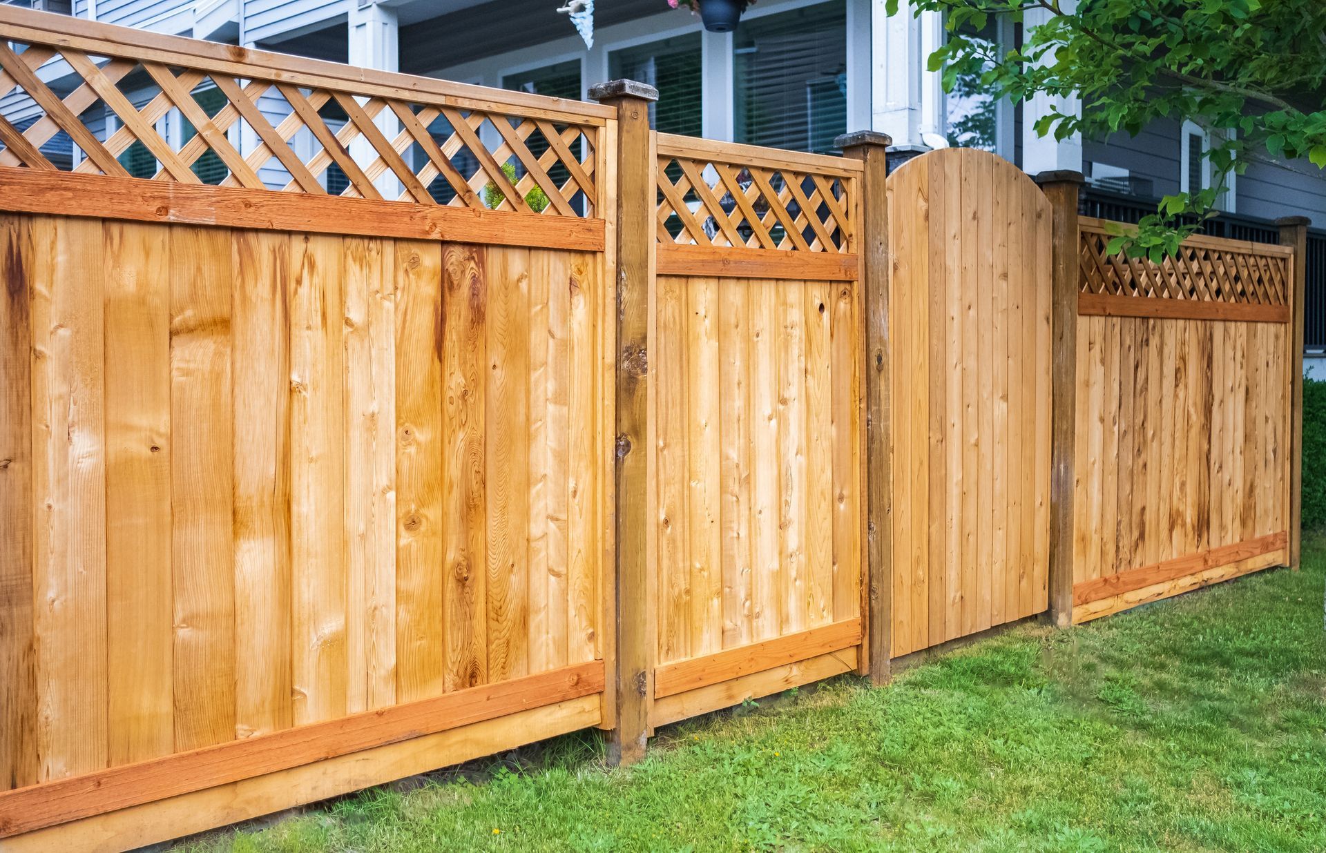 A wooden fence around the house, with a green lawn, installed by a fence contractor.