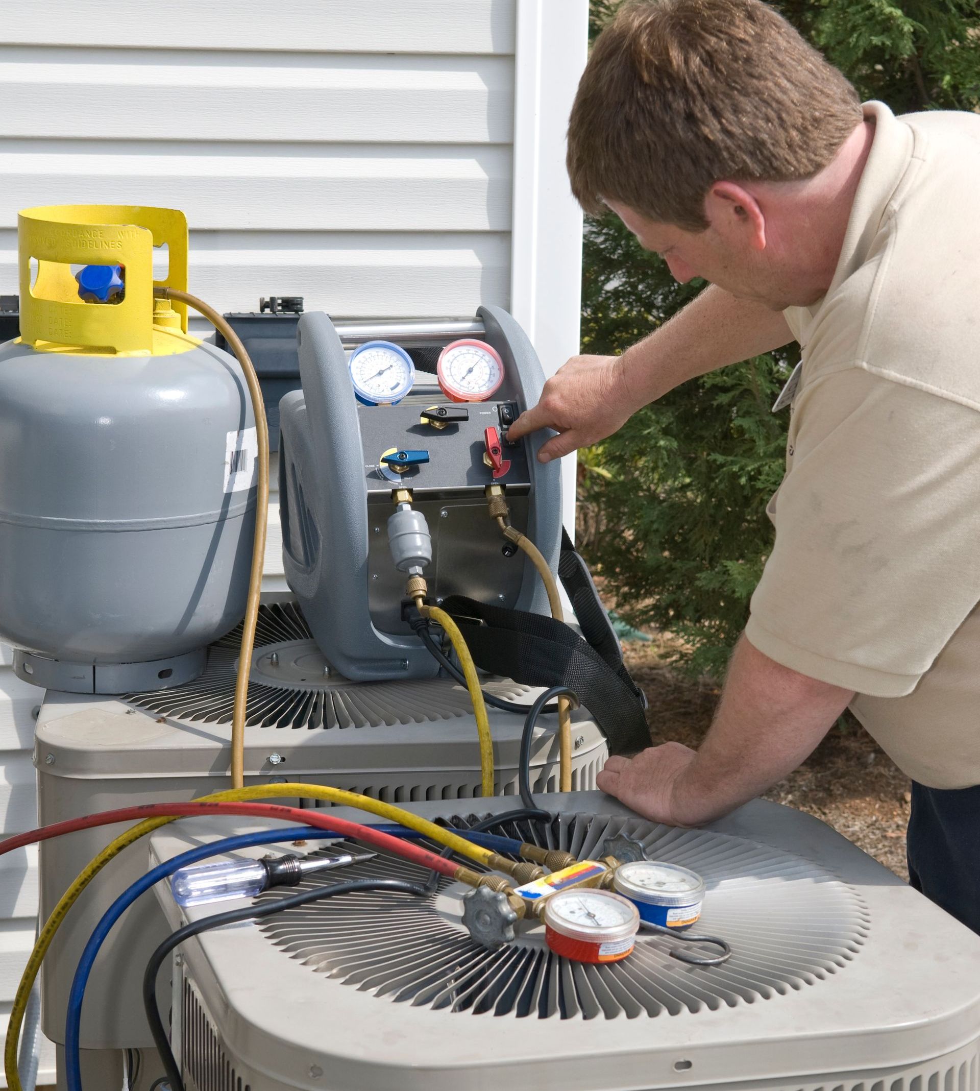 A professional AC repairman charges a residential central air conditioner unit with refrigerant (Freon) to restore proper cooling functionality.