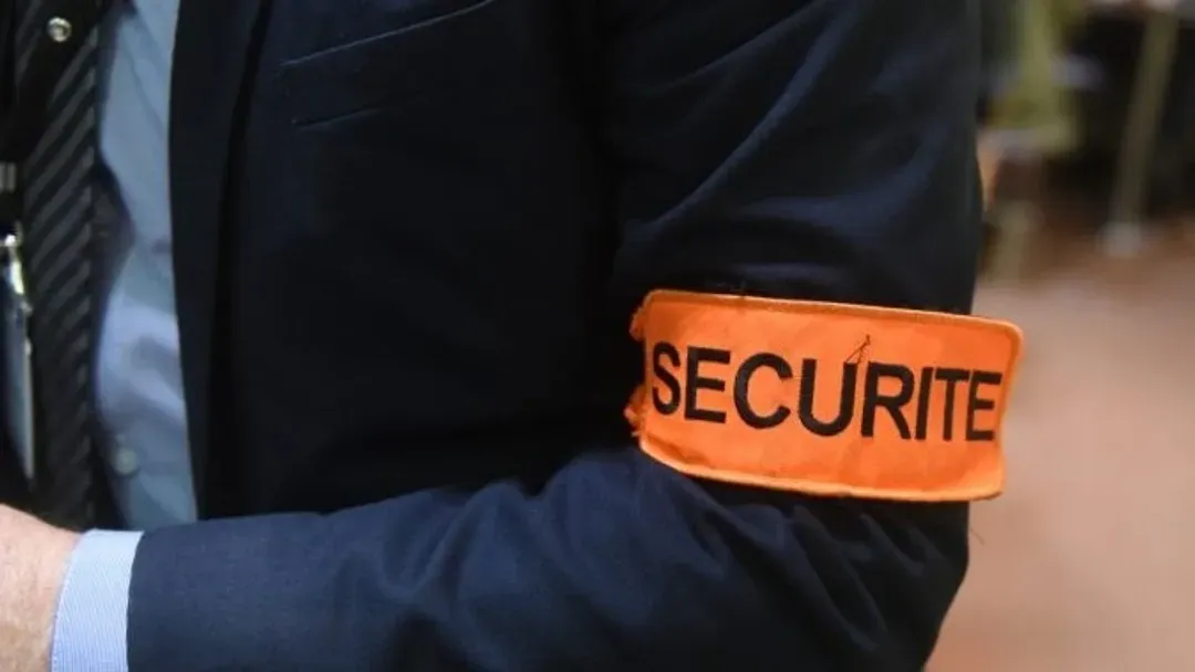 Un homme en costume porte un brassard orange avec le mot sécurité dessus