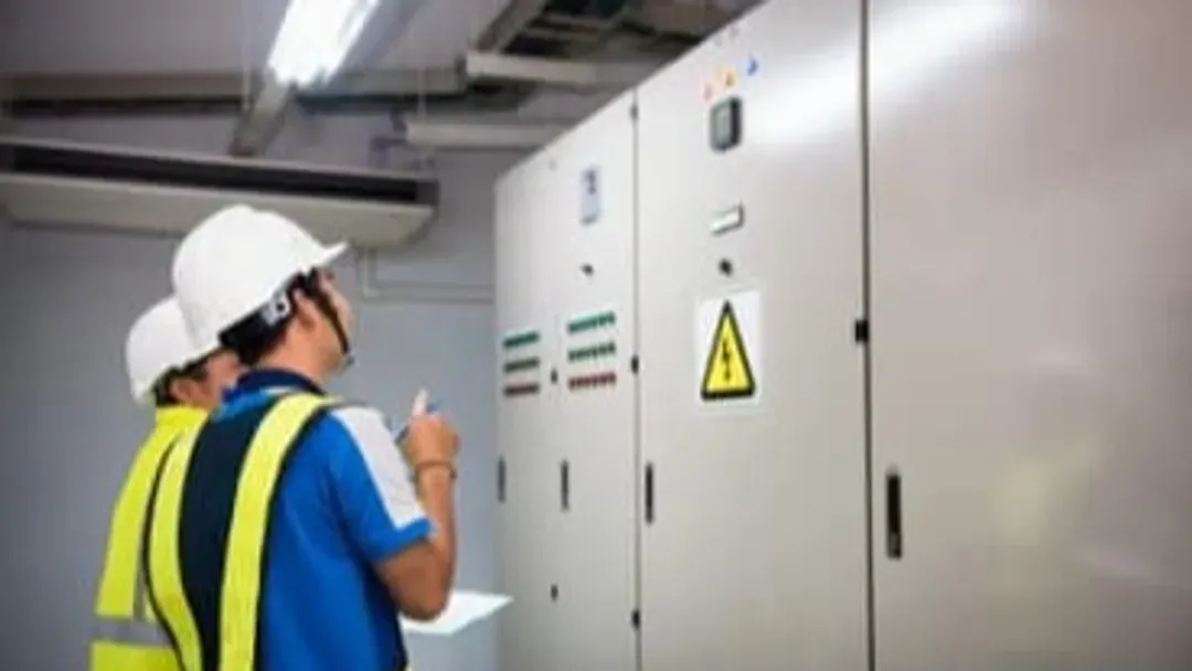 Deux hommes portant des casques de sécurité et des gilets de sécurité regardent un boîtier électrique.