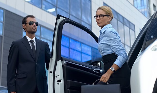 Un homme en costume et cravate se tient à côté d'une femme qui sort d'une voiture.