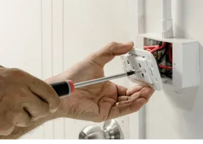 Une personne répare une prise électrique avec un tournevis.