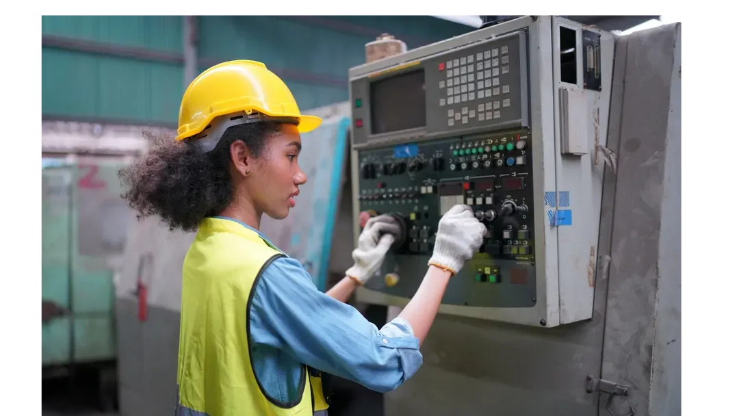 Une femme portant un casque et un gilet de sécurité travaille sur une machine dans une usine.