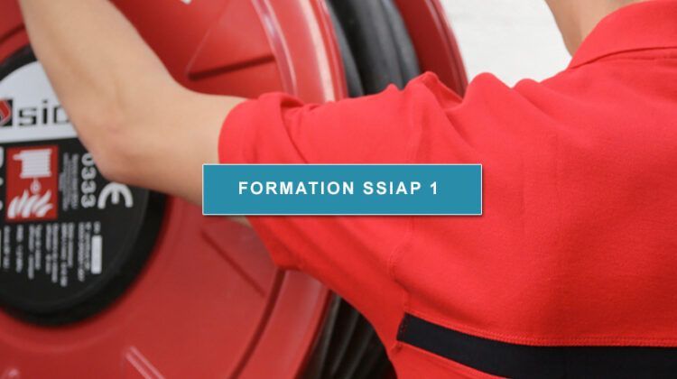 Un homme en chemise rouge tient un grand objet rouge devant un panneau indiquant formation ssiap 1