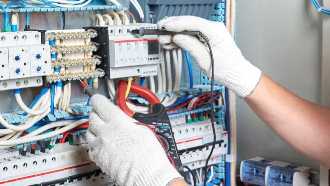 Un électricien travaille sur un coffret électrique avec un multimètre.