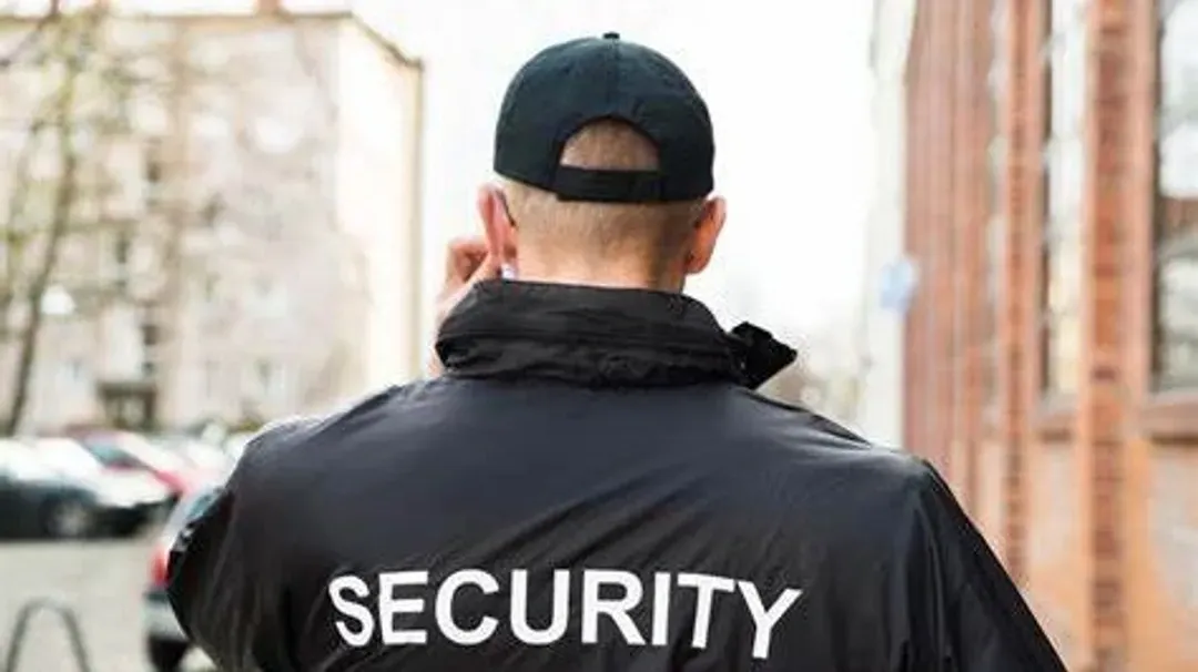 Un agent de sécurité parle au téléphone portable tout en portant une veste noire et un chapeau.