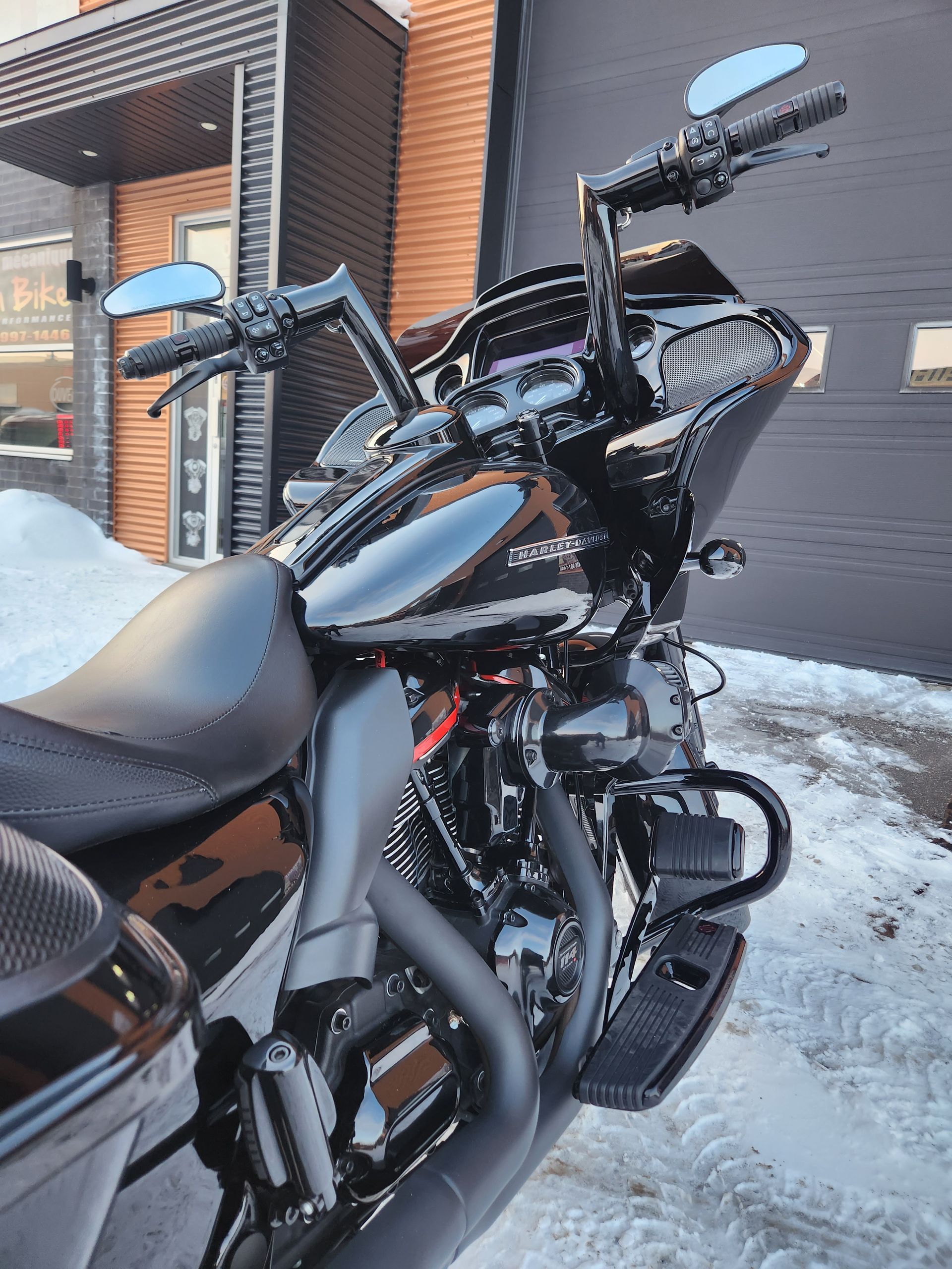 Moto Harley-Davidson noire garée devant un bâtiment par une journée enneigée.