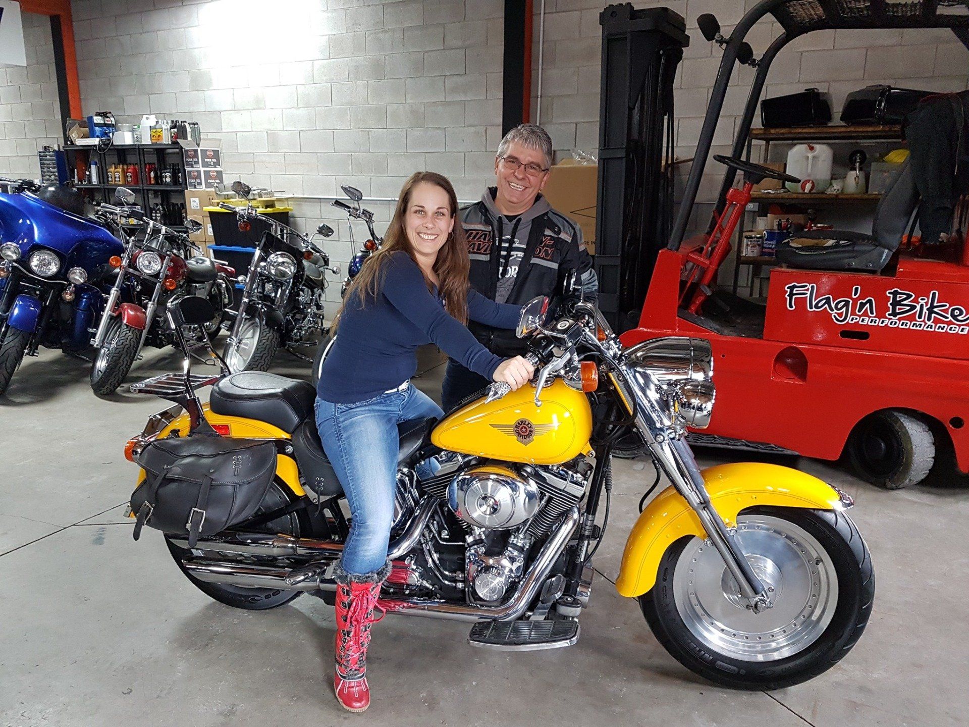 Une femme assise sur une moto jaune ; un homme se tient à côté d'elle dans un garage.