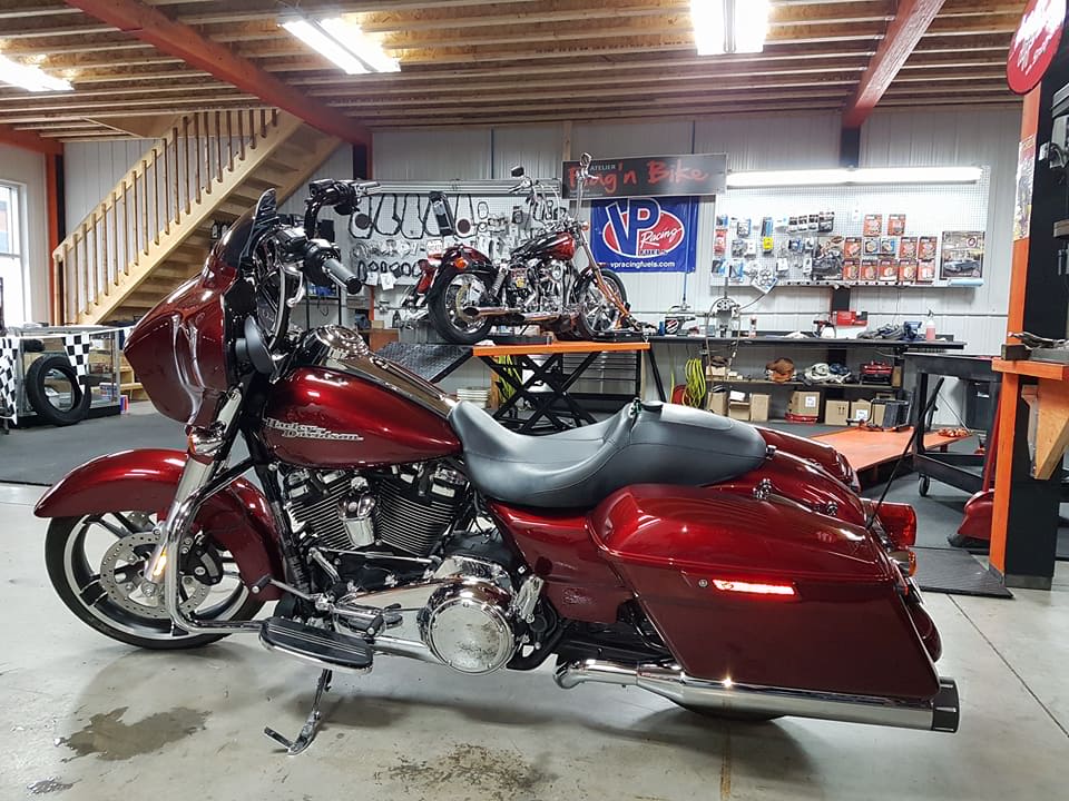 Moto Harley-Davidson rouge dans un magasin ; autres motos et outils en arrière-plan.