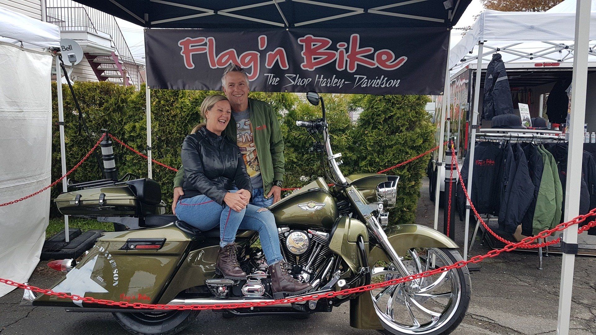Deux personnes posent avec une moto verte personnalisée sur le stand d'un vendeur, « Flag'n Bike ».