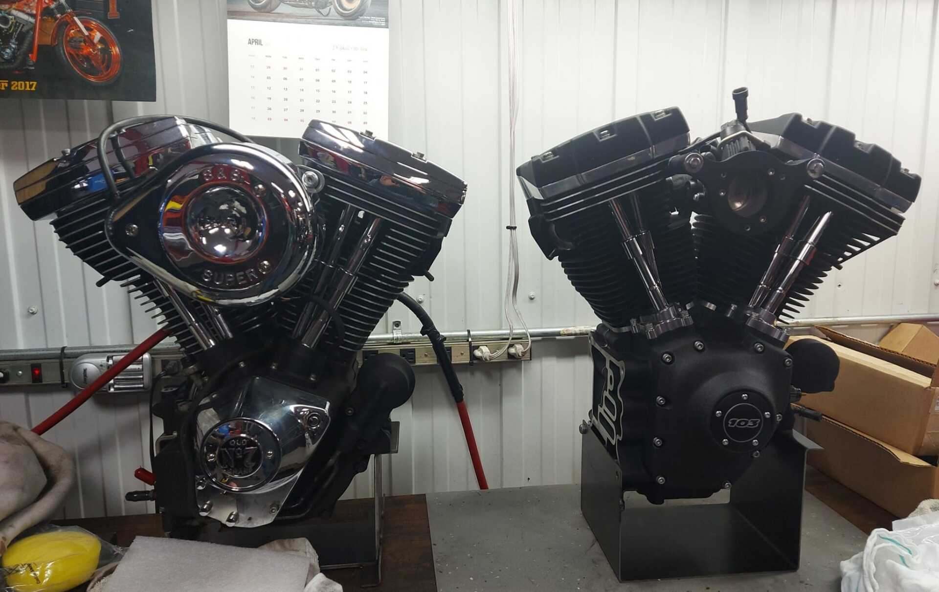 Deux moteurs de moto bicylindre en V, l'un chromé, l'autre noir, sont placés côte à côte dans un atelier.