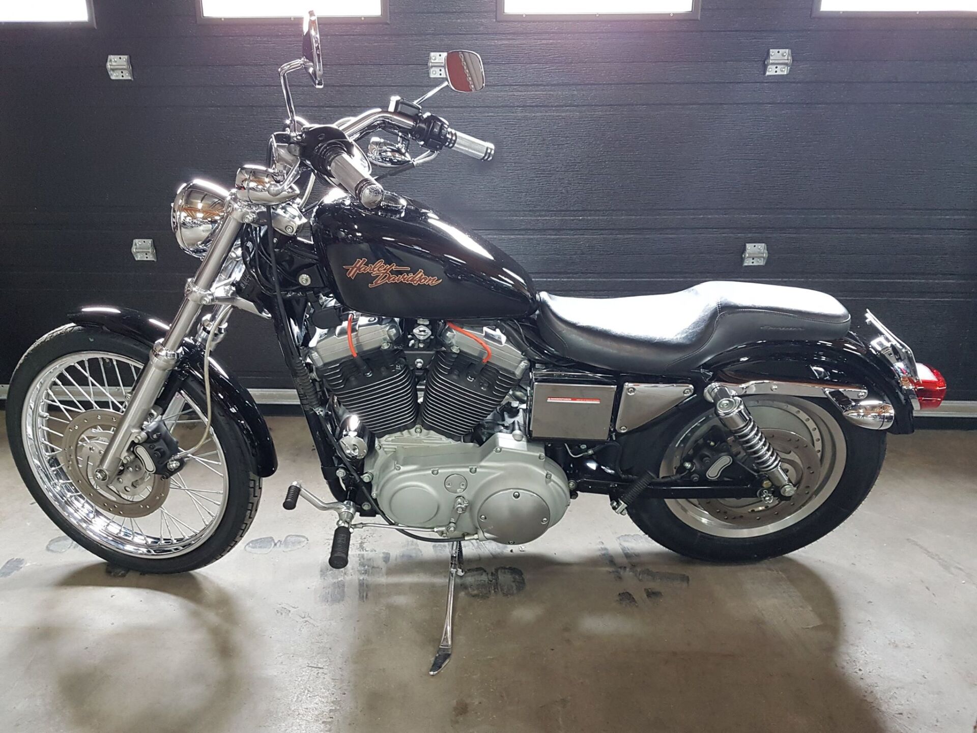 Moto Harley-Davidson noire avec détails chromés garée à l'intérieur contre un mur sombre.