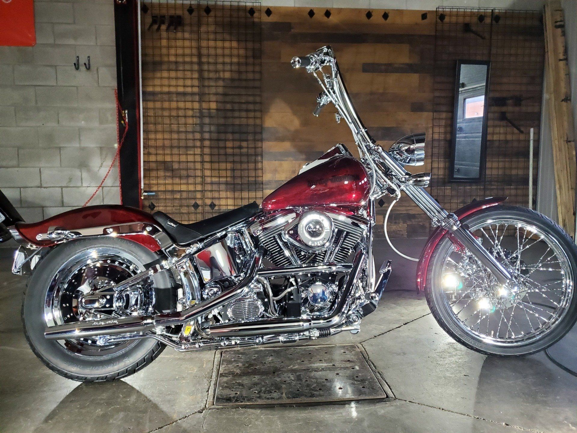 Moto custom rouge brillant et chromée avec guidon haut, garée à l'intérieur.