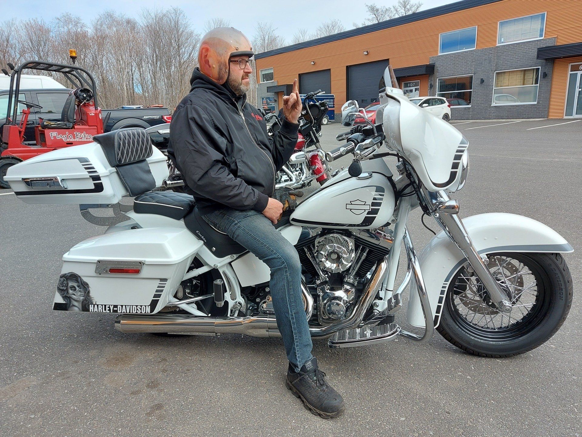 Un homme sur une moto blanche, portant une veste noire et un jean, à l'extérieur, pointant vers le haut.