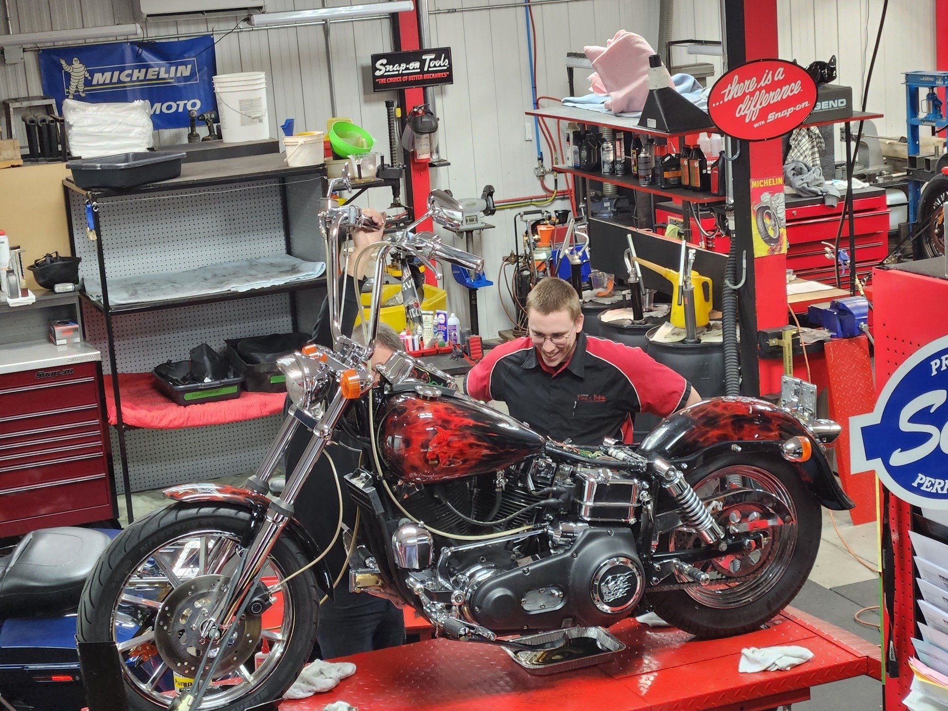 Mécanicien travaillant sur une moto customisée dans un atelier. Couleurs rouge et noir.