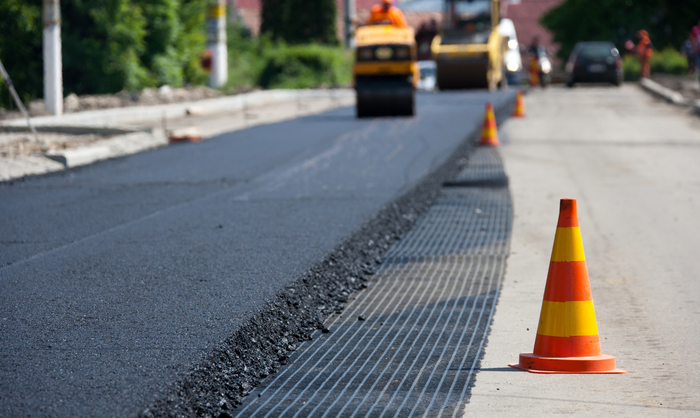 Road paving in progress, with a steamroller and orange traffic cone on the side.