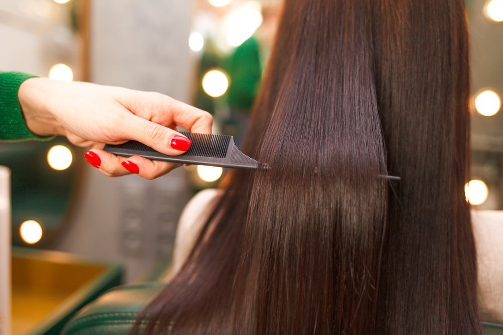 A Woman is Getting Her Hair Straightened by a Hairdresser — Choo Choo Hair and Beauty In Wyong, NSW