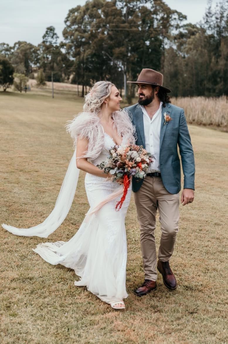 A Bride and Groom Are Walking Through a Grassy Field Holding Hands — Choo Choo Hair and Beauty In Wyong, NSW