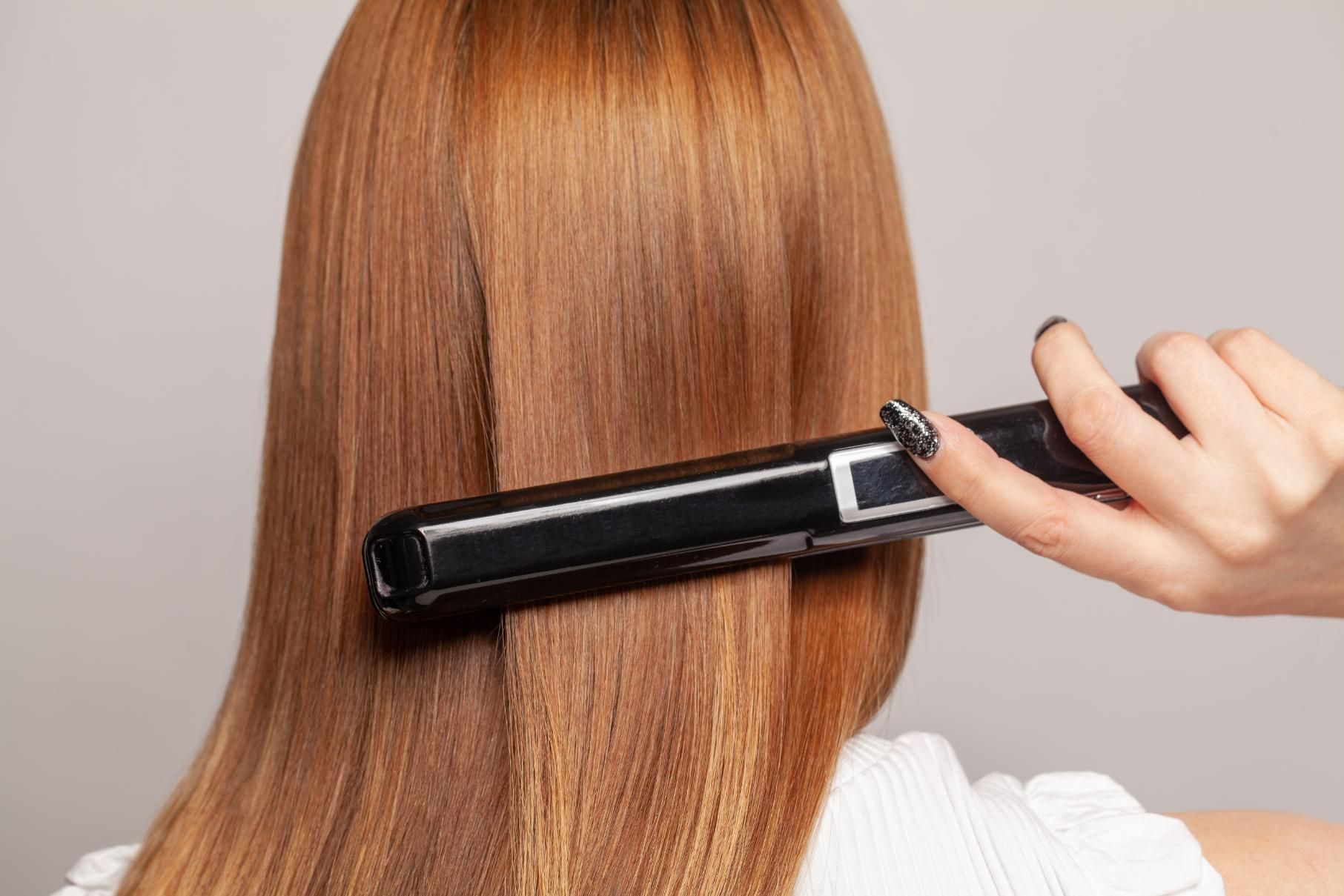 A Woman is Getting Her Hair Straightened With a Flat Iron — Choo Choo Hair and Beauty In Wyong, NSW