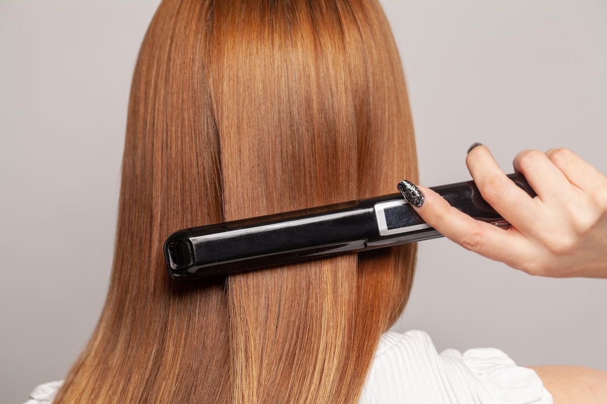Person Straightening Brown Hair With a Black Flat Iron — Elysian Salon In Wyong, NSW