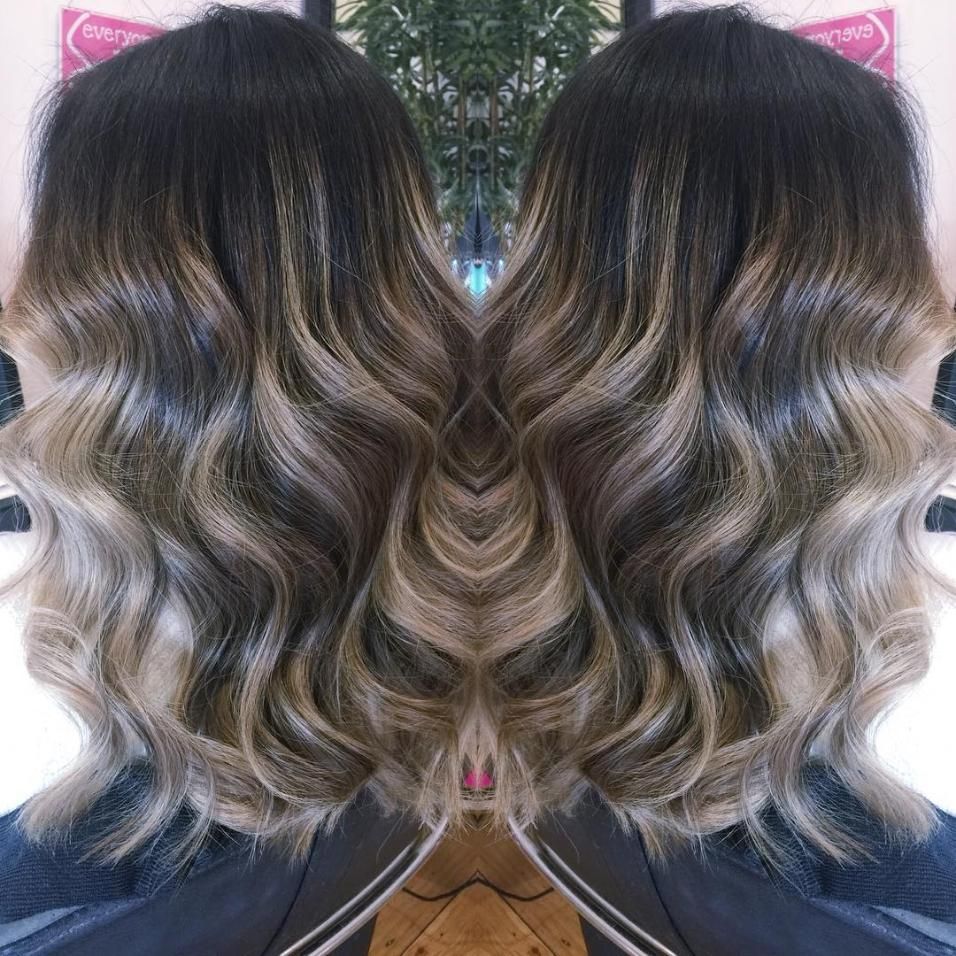 A Woman With Long Wavy Hair is Standing in Front of a Mirror — Choo Choo Hair and Beauty In Wyong, NSW